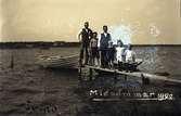Midsommar 1922 på Svinö. Folk som står på en liten brygga med småbåtar förtöjda.