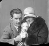 En kvinna i hatt och päls, en man i kostym och en hund med koppling till Hirschs Pianomagasin.