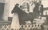 Friherrinnan Ebba Thott med svärdotter och barnbarn. Barnet sitter på en ponny på uteplatsen utanför mangårdsbyggnaden.