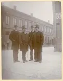 Fyra herrar varav två har plommonstop och två har cylinderhatt. De är klädda i rock. Två av dem har käpp.