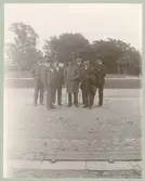 Herrar i kostym, rock, hatt och käpp. Gamla vattentornet syns i bakgrunden.