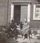 En drängstuga på Öland. Björkerum 5. En man, kvinna och hund sitter på trappan utanför dörren.