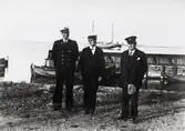 Tre herrar, varav en uniformsklädd, stående vid hamnen på Revsudden.