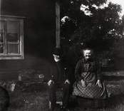 Kalle Bäck med hustru sittande vid stugknuten.