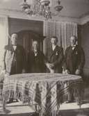 Fyra herrar, stående vid ett bord.