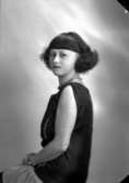 Ateljébild på en kvinna i armbandsur, pärlhalsband och klänning. Enligt Walter Olsons journal är bilden beställd av fröken Astrid Bergquist.