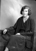 Ateljébild på en kvinna i halsband, blus och jacka. Enligt Walter Olsons journal är bilden beställd av Astrid Hansson.