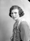 Ateljébild på en kvinna i pärlhalsband och klänning. Enligt Walter Olsons journal är bilden beställd av Anna Johansson.