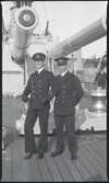 Två sjöofficerare med fänriks grad poserar på däck under tungt artilleri på pansarskepp; till h Gunvald Berger.