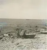 Kåsar vid stranden. Fiskebåt drages ut. I fören ligger råseglet hoprullat.
