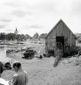 Vy med sjöbod mot söder och kyrkan i bakgrunden.