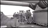 Kvinnor och flottister på däck under kanonerna, på ett pansarskepp. Andra bilder i Gunvald Bergers samling tyder på att denna bild tagits under flottuppvisningen i Göteborg 1929, men denna förmodan har inte kunnat bekräftas.