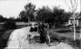 Georg Skatt med sin syster Signe i sidovagnen. På landsvägen vid Furåsen. Motorcykeln av märket Indian. I bakgrunden Skatss verkstad och smedja.