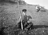 En ung jägare, troligen Ernst Bauer, sitter med en hund på en grässluttning.