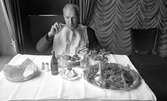 Kräftor 9 augusti 1967

En man med vit servett över hela bröstet sitter och äter kräftor vid ett bord med vit duk på. Han har ett ölglas samt ett snapsglas på bordet framför sig. Även en flaska öl, ett brödfat, salt och peppar, ett litet fat med smör samt ett silverfat med ytterligare kräftor står där.