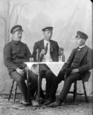 Ateljé. 
Tre herrar med flaskor och glas på bordet. 
Fotograf: Ellen Kock? Axel Lundbäck m.fl.