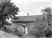 Exteriör. Fyra damer och en herre framför lågt hus med enkel veranda. Gullspångssamlingen. Bilder från Gullspång med omnejd.