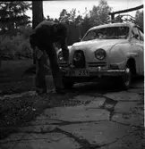 Bilen på bilden är en SAAB 93 eller 96, före 1964.
Med tanke på att bilden saknar huvemblem borde det vara en 96a från -63 eller -64. Bilden måste dock vara från 1971 eller senare då den har modern nummerplåt.