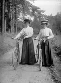 TVÅ KVINNOR MED CYKLAR OCH VAR SIN BLOMBUKETT I HÄNDERNA.