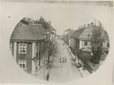 Östra Sjögatan på 1870-talet, sedd från Kavaljeren. I förgrunden till vänster Kv Borgmästaren (Östra Sjögatan 1) i dess ursprungliga skick: Väggar panelade och röda med vita knutar, taklist med träsnitt. Framför huset i gatkanten en lind. I fonden skymtar Kantorsporten, en av de nu rivna portarna i Kalmars stadsmur. Framför porten syns eventuellt en av stadens brunnar.