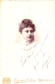 Bröstbild av Ellen Warholm som flicka i vit klänning med hög krage eller scarf om halsen. Handskriven text på kortet: Till Mamma julafton 1895 från din Ellen.