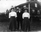 Två damer i stora hattar, en man.
