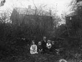 Fyra barn och en vuxen sittandes i en trädgård.