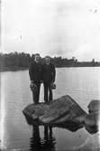 Två män på stenblock vid strandkanten till sjö.