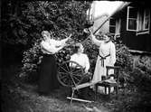 Kvinnor i svarvare Holms trädgård med spinnrock och vattenkanna, Östhammar, Uppland