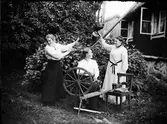 Kvinnor i svarvare Holms trädgård med spinnrock och vattenkanna, Östhammar, Uppland