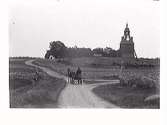 Landskap med kyrka och hästskjuts vid vägskäl. 1890-tal.
