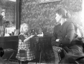 Kvinna med lekande barn. Fotografen Nanny Ekström kan ses i spegeln.