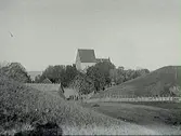 Gamla Uppsala kyrka i Uppland med hankgärdesgårdar och en av högarna i förgrunden.