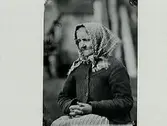 Kvinnoporträtt. Sittande gumma med knäppta händer. Troligen Elna Bengtsson som bodde i södra Björsgård.