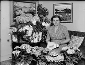 Kvinna i bostadsmiljö omgiven av blommor, Östhammar, Uppland