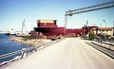 Ett fartyg på en stapelbädd på varvet i Kalmar. Under en kran och en bockkran.