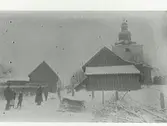 Laholms kyrka. Snöbild. På vägen mellan huset står folk och pratar. Två pojkar med kälkar. Vid vägen ligger rishögar.
