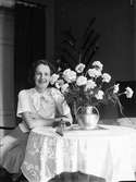 Ung kvinna sitter vid bord med blommor 1930-40-tal, sannolikt i hemmet , Sverige