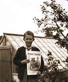Allan Molin i Vabränna by står framför ett växthus och håller upp tidningen Hemmets Journal, som han säljer för 30 öre.