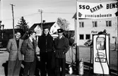 Fyra herrar vid en bensinpump på Esso i Veddige. Fr. v Lennart Tjärnmo, Erland Gustafsson, Kennet Tjärnmo och till höger mackägaren Henry Svensson. I bakgrunden syns Postkontoret.