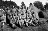 En grupp militärer och tält i en skogsbacke. Till höger skymtar en cykel. Bilden är troligen tagen under beredskapstiden vid andra världskriget. Fotografen själv gjorde beredskap vid Radiostationen i Grimeton, så möjligen är bilden tagen i samma socken.