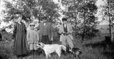 Familjen Lundgren i Ry poserar finklädda i gröngräset med två hundar framför en späd trädridå. Sonen Anders håller en kikare om halsen. Alla utom fadern bär långrandiga kläder; moderns hellånga klänning har en sidoknäppning.