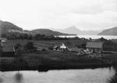 Gårdar längs fjord, fjällen i bakgrund, sannolikt Norge