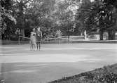 Två ungdomar, flicka och pojke stående på tennisbana med tennisracket i handen, sannolikt i Sverige