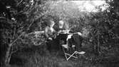 Christiane Liljefors föräldrar Roland Petersen och Pauline Egelind Petersen läser tidning i trädgård, sannolikt i hemmet 