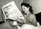 En skådespelerska läser tidningen i sängen.
