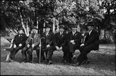 Sex män sitter på en parkbänk iförda kostymer och hatt. Alla har de en knapp på kavajslaget, en medalj.  F d mjölnaren Betania-Johannes i skägg och August Johansson i Darragården har varsin käpp, Längst till höger sitter Karl Larsson i Albäck och övriga är Martin på Ledet, Johan Barkhult och ytterligare en Johan.