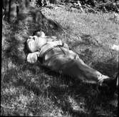 En man ligger i skuggan vid ett träd och vilar med händerna knäppta på magen.