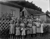 Sexton flickor (möjligen en pojke) på Kerstin Johanssons 10-årskalas den 18 augusti 1939 i Albäck. De står på utsidan av trädgårdens vitmålade trästaket, varöver dahlior, rosor och andra sensommarblomster skjuter upp. Slipens Klas står baktill i hatt och kostym.
Bland barnen syns bland annat Margit Larsson, Gerda Johansson på Nytorp, Lundgrens Ella (fosterbarn hos Anders Lundgren), Inga i Kantabur, Anna Greta i Kantabur, Karin på Nytorp (Larsa Karin) och 