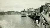 Ångbåten Gustavsberg VI förtöjd vid i Gustavsbergs hamn. Båten byggdes 1896. Gula byggningen skymtar till höger, i bakgrunden Värdshuset och i fjärran Statbyggningen och Ekensberg.